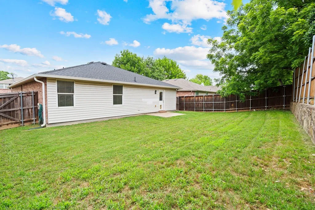 Expansive backyard featuring a manicured lawn, a privacy fence, and a stone retaining wall