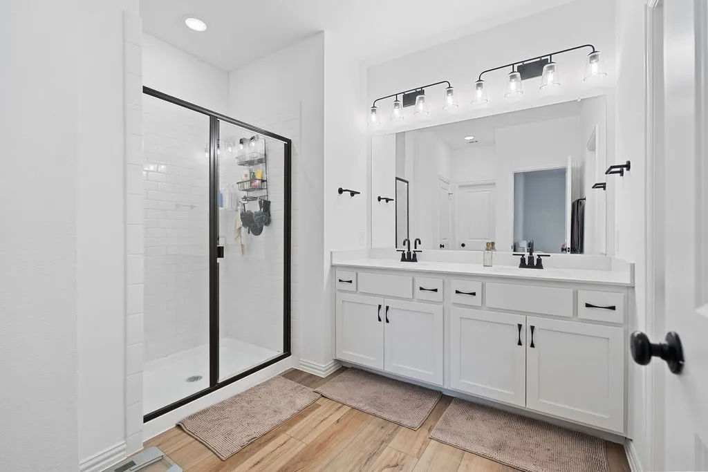 Contemporary bathroom featuring a dual vanity with white cabinetry, matte black hardware, and an expansive mirror