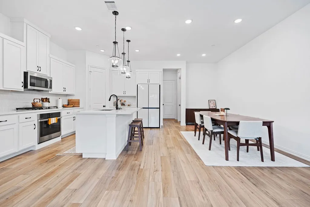 Bright kitchen featuring white cabinetry, a large center island with seating, stainless steel appliances, and wood-finish flooring throughout