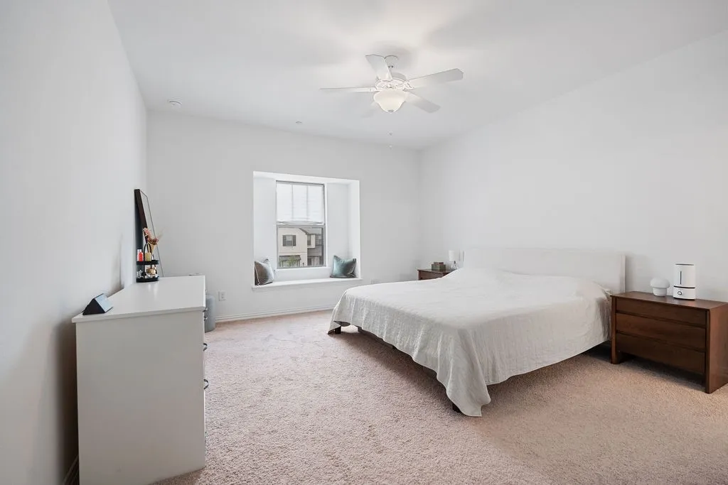Carpeted bedroom featuring a window seat with built-in storage, a ceiling fan with light fixture, and white painted walls