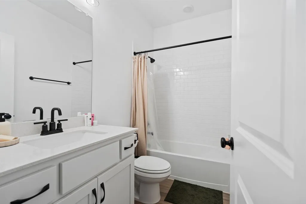 Bathroom featuring a white vanity with an integrated sink, matte black fixtures, a full-width mirror, subway tile shower surround, and wood-finish flooring