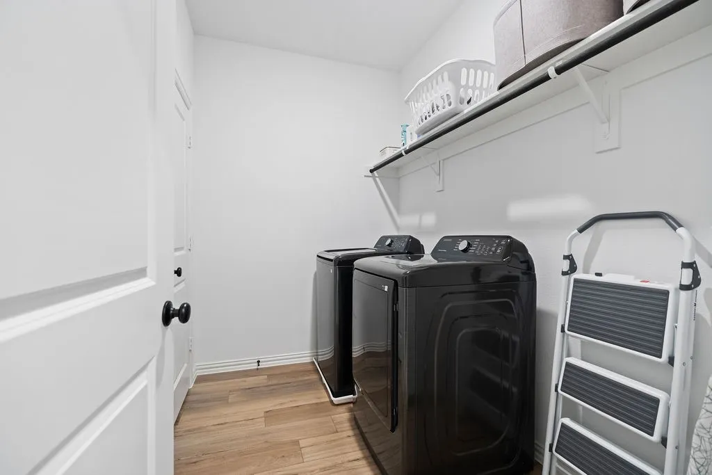 Dedicated utility area featuring wood-finish flooring, white walls, and a white paneled door with matte black hardware