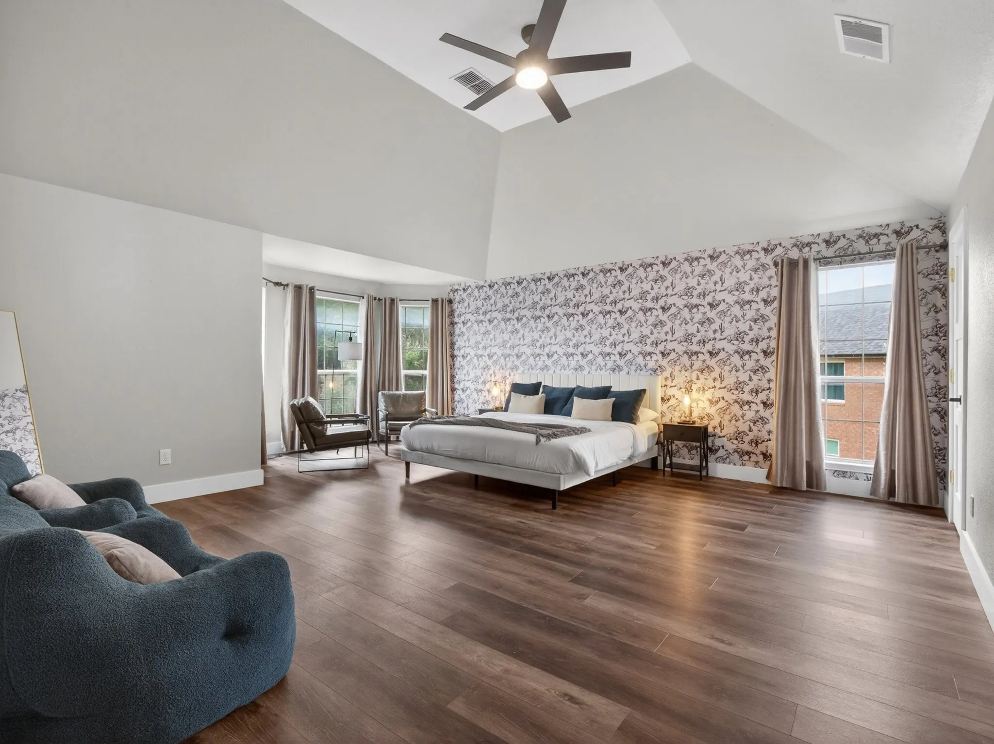 Spacious room featuring wood-finish flooring, a vaulted ceiling with a ceiling fan, and a patterned accent wall