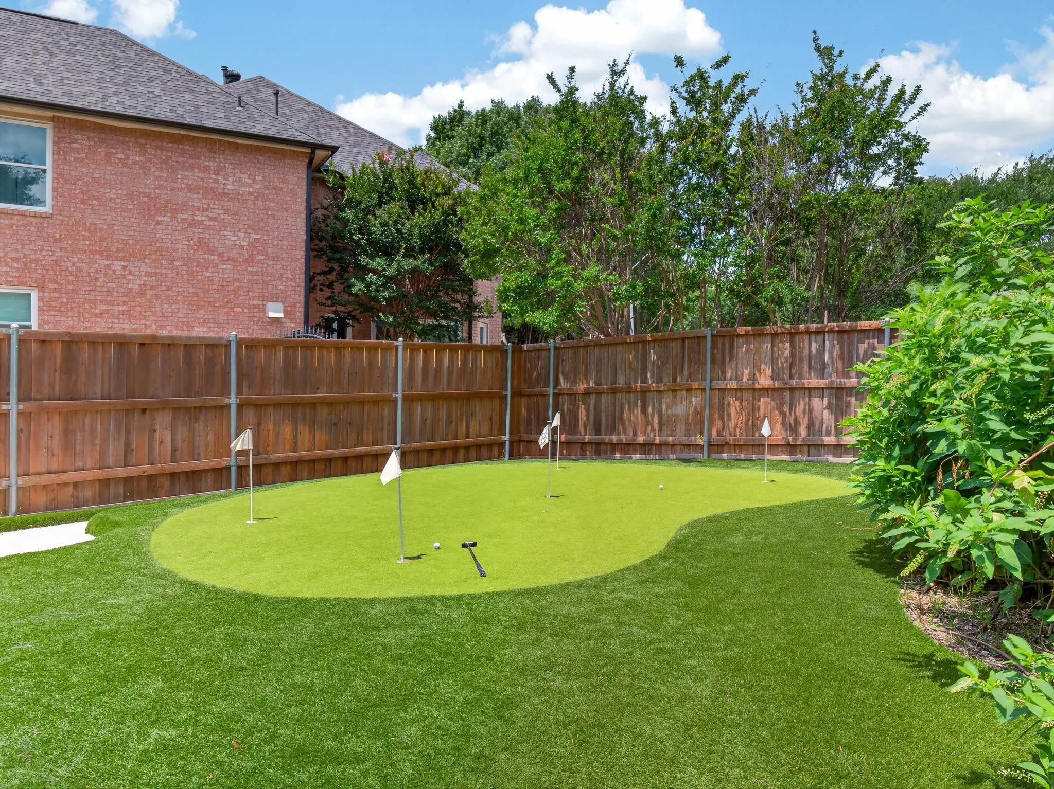 Expansive backyard featuring a private putting green with multiple holes, artificial turf, and a perimeter wood privacy fence