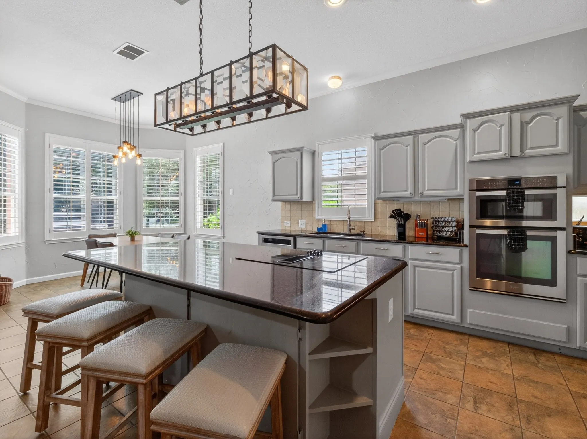 Kitchen featuring a large island with cooktop, gray cabinetry, built-in double ovens, and tile flooring