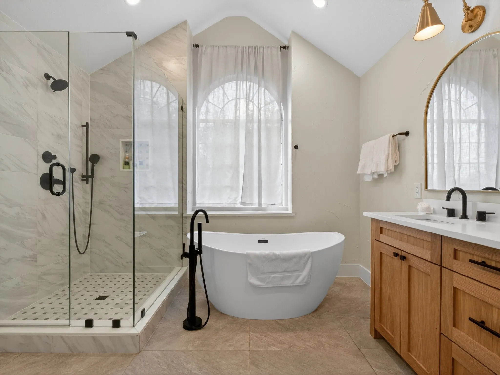 Spacious bathroom featuring a frameless glass shower enclosure, a freestanding soaking tub with floor-mounted faucet, and an arched window