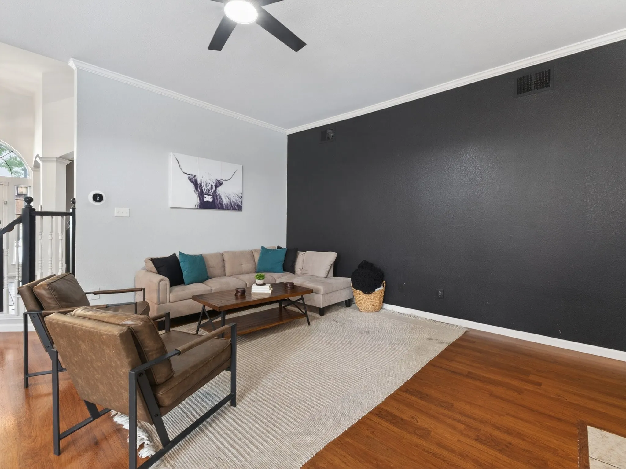 Spacious living area featuring wood-finish flooring, a ceiling fan, and crown molding
