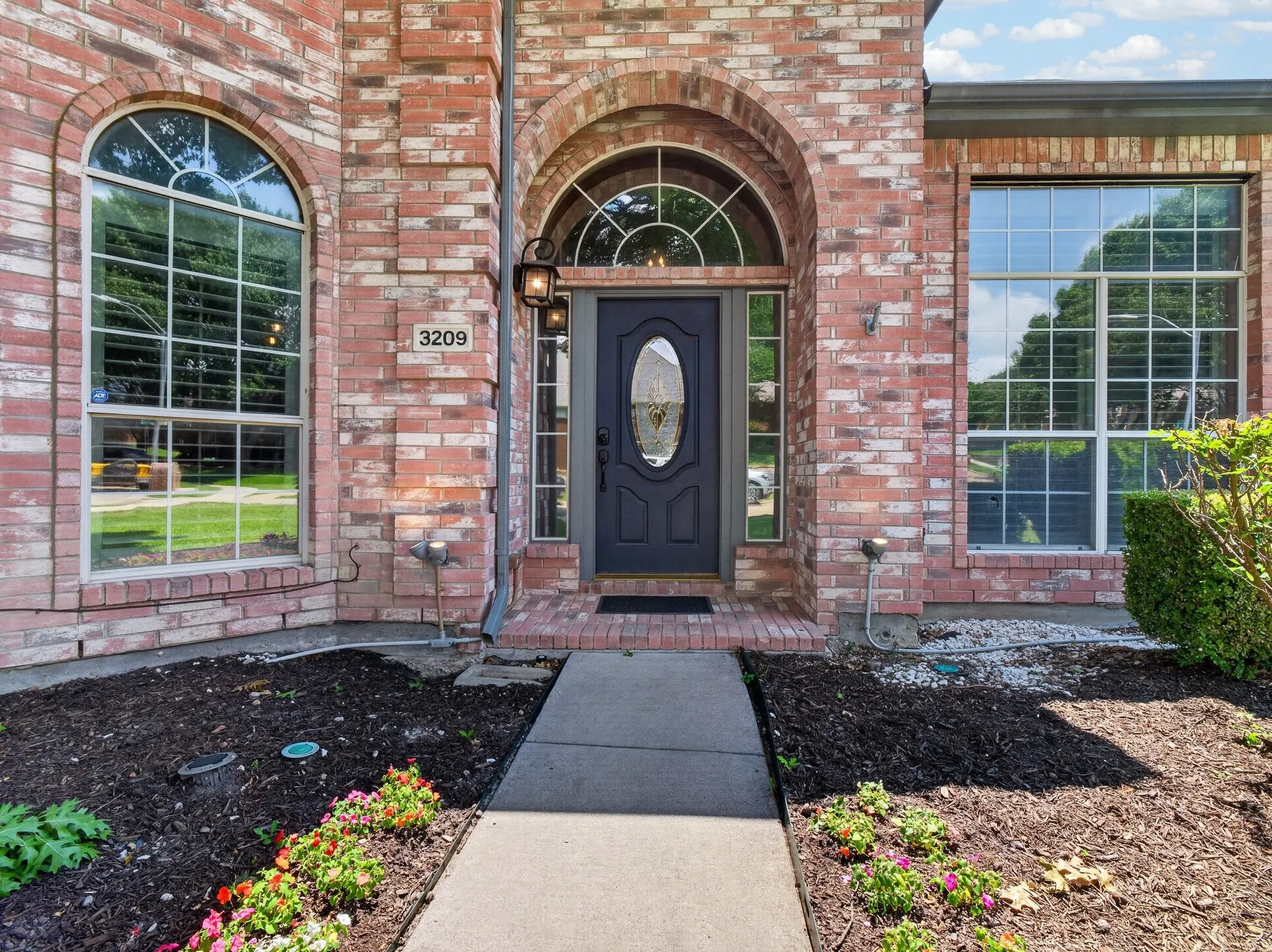 Brick facade entry featuring an arched front door with decorative glass, two sidelight windows, and an arched transom window