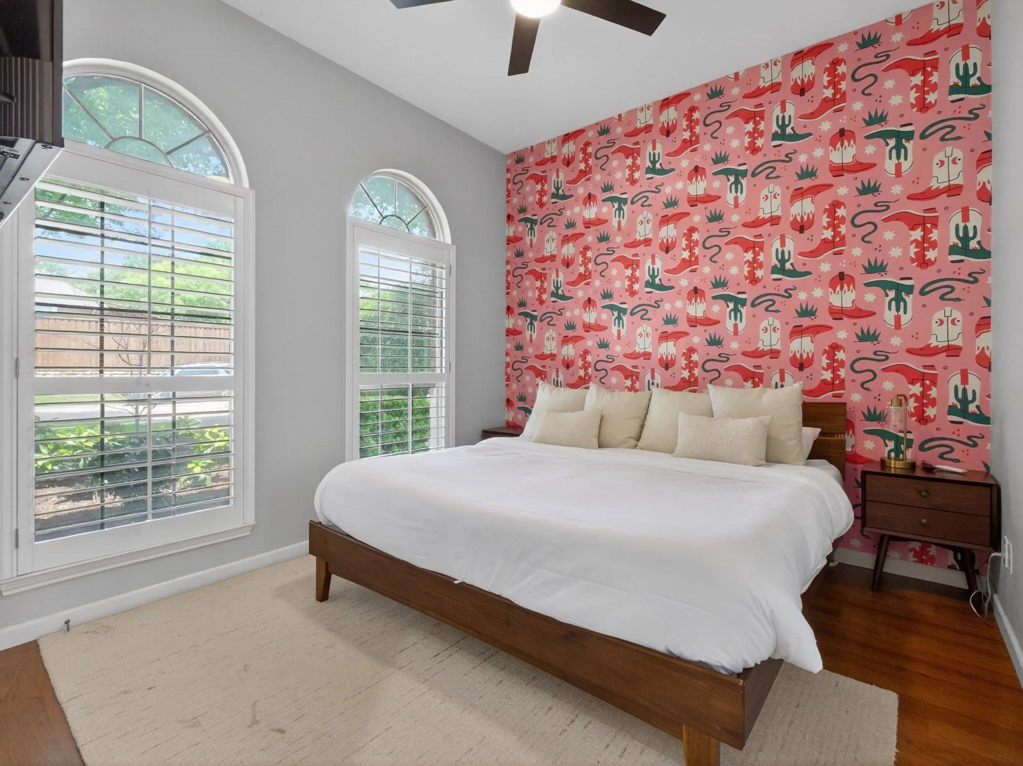 Interior room featuring dual arched windows with plantation shutters, a decorative accent wall, wood-finish flooring, and a ceiling fan