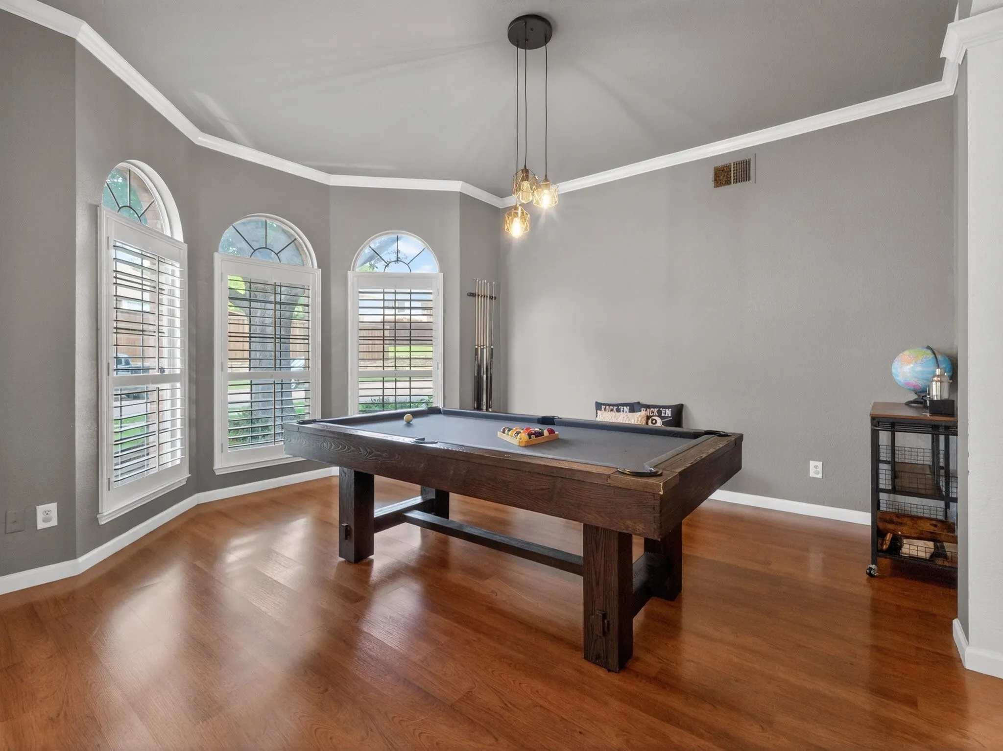 Bay window with three arched windows and white plantation shutters, rich wood-finish flooring, and crown molding