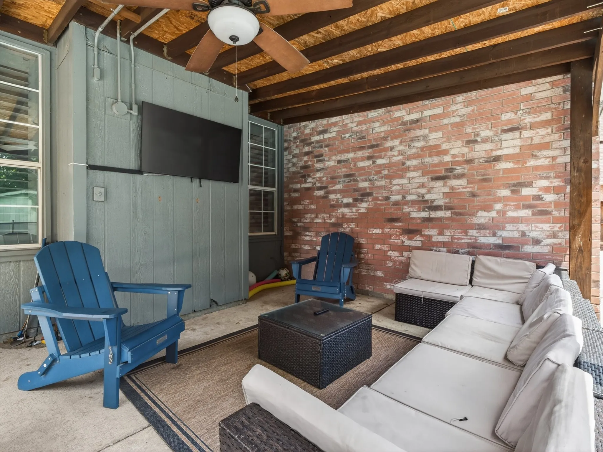 Covered patio featuring a ceiling fan with integrated lighting, brick accent wall, wood-paneled ceiling, and concrete flooring