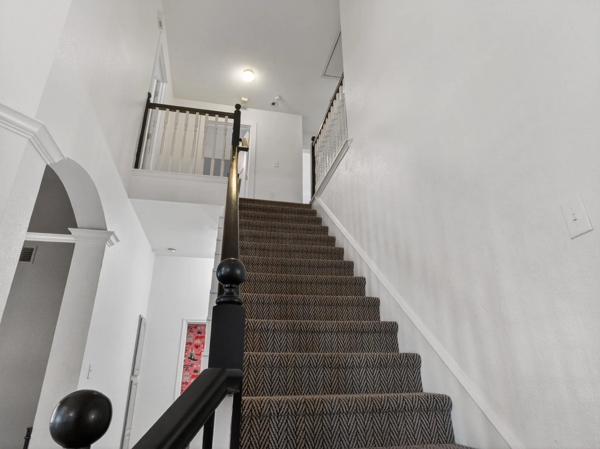 Carpeted staircase with dark wood newel posts and railings, white balusters, and an arched entry