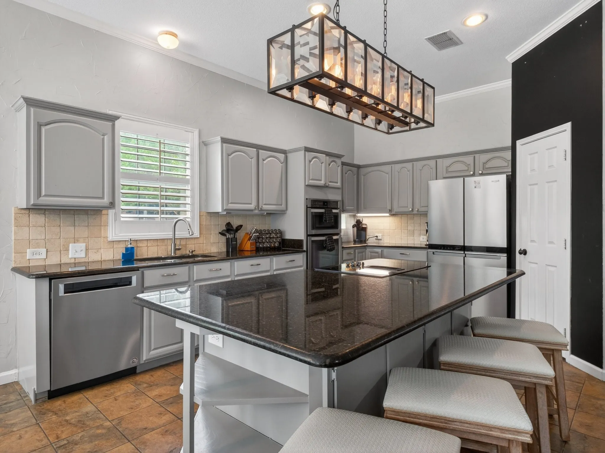 Kitchen featuring an island with a dark countertop, light gray cabinetry, stainless steel appliances, tile backsplash, and ceramic tile flooring