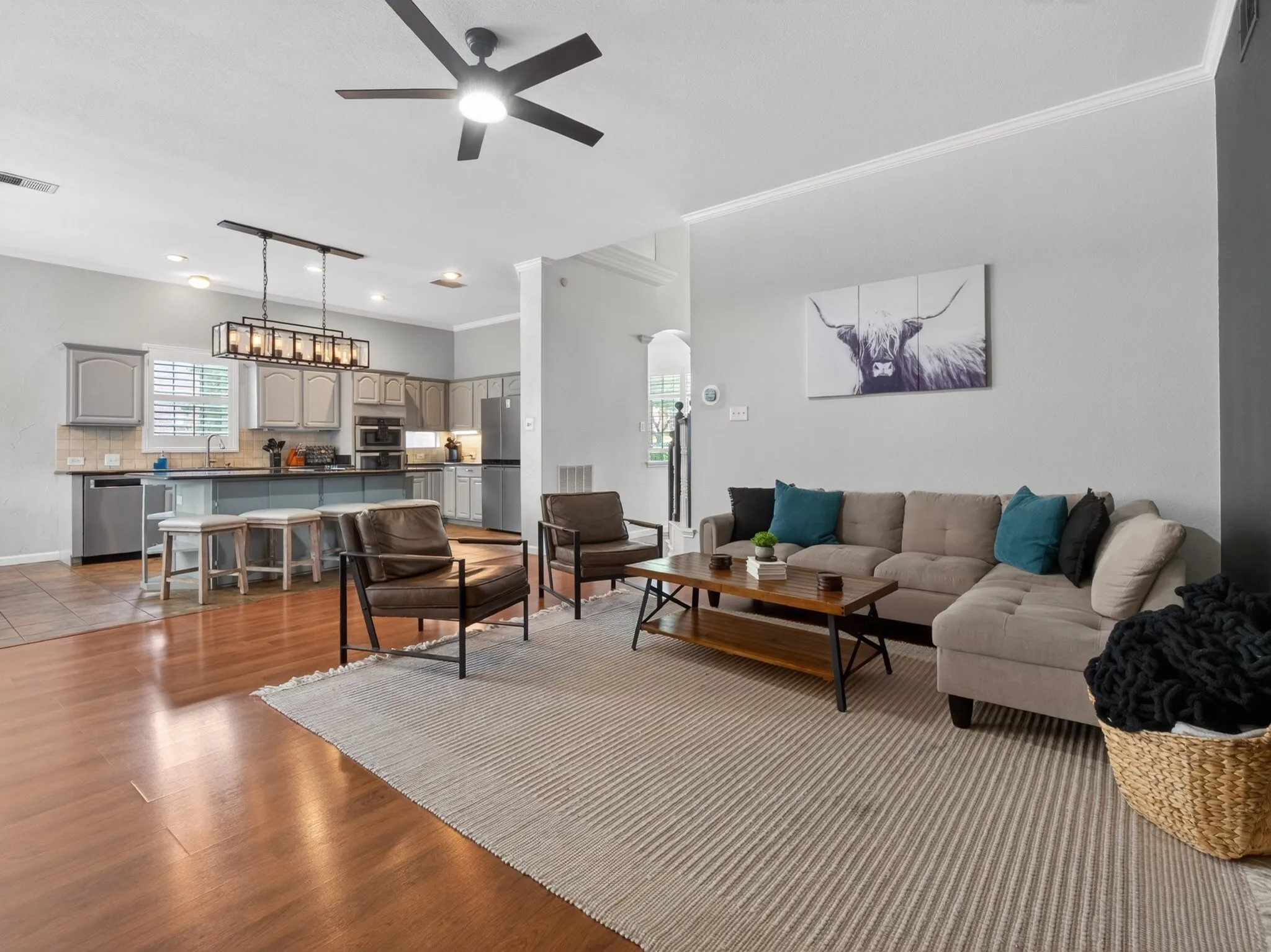Open-concept living area featuring wood-finish flooring, a contemporary ceiling fan, and crown molding