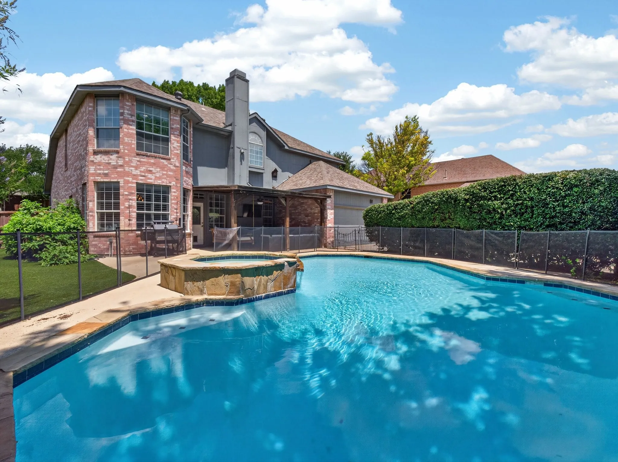 Backyard oasis featuring a large swimming pool, integrated spa with natural stone accents, and a safety fence enclosure