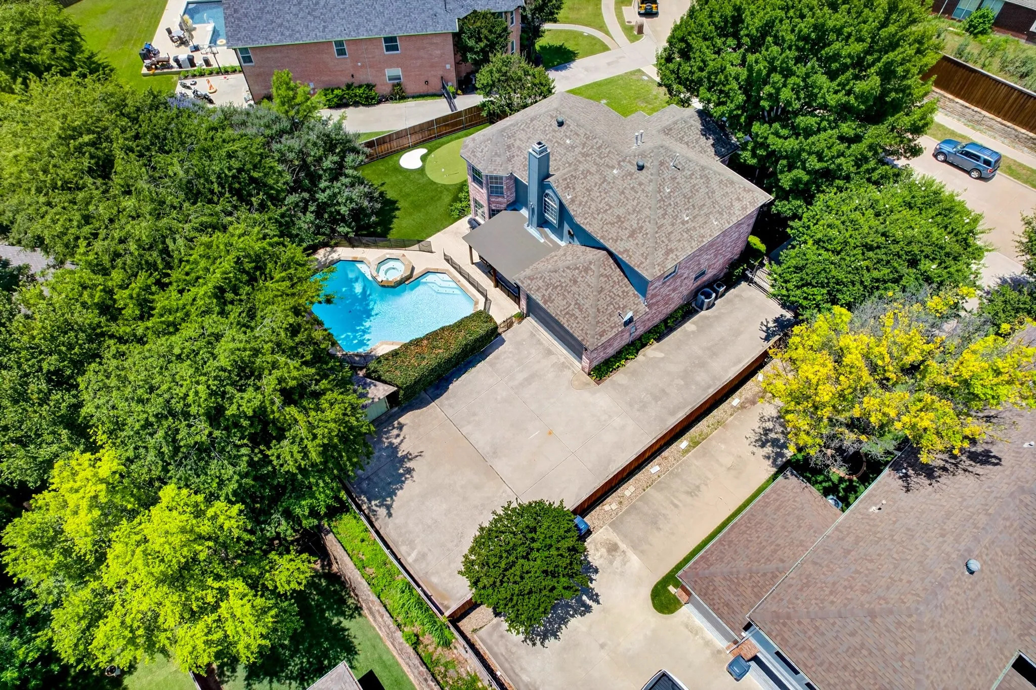 Aerial view highlighting the property's exterior amenities, featuring a kidney-shaped swimming pool with an integrated spa, a concrete patio surround, and a putting green
