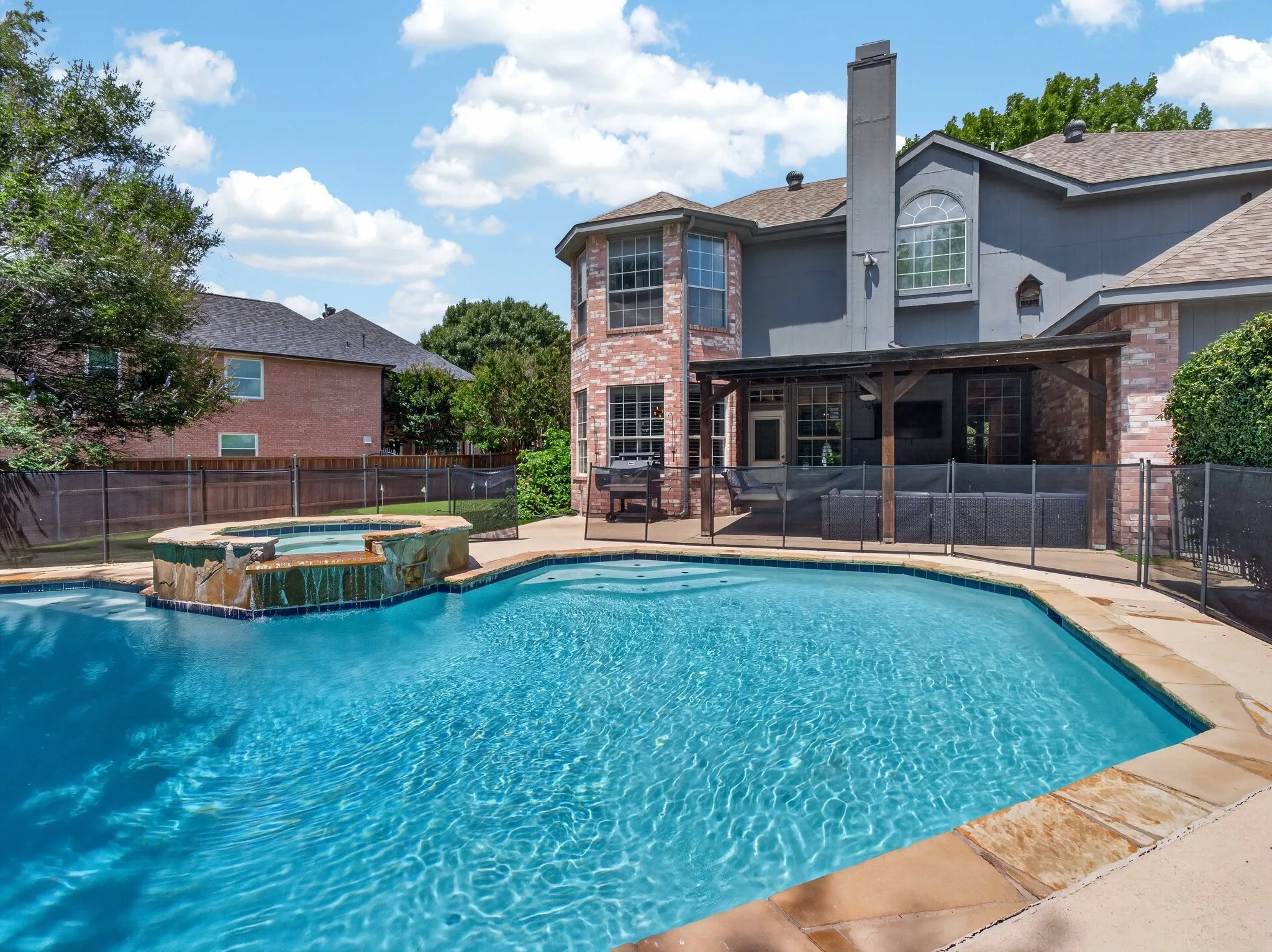 Expansive backyard with a sparkling pool featuring a spa with a waterfall, surrounding concrete patio, and a covered patio structure