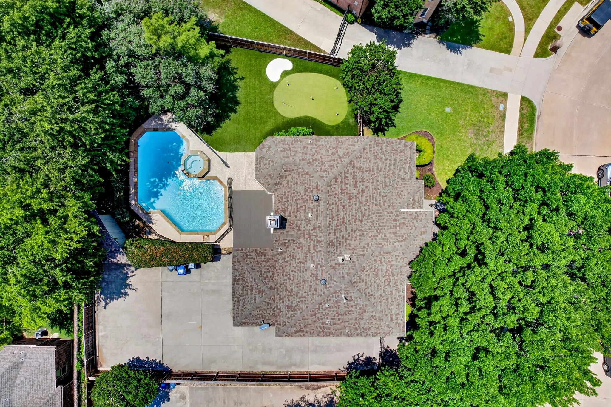 Aerial perspective showcasing a private backyard oasis featuring a swimming pool with integrated spa, a dedicated putting green, and extensive concrete patio space