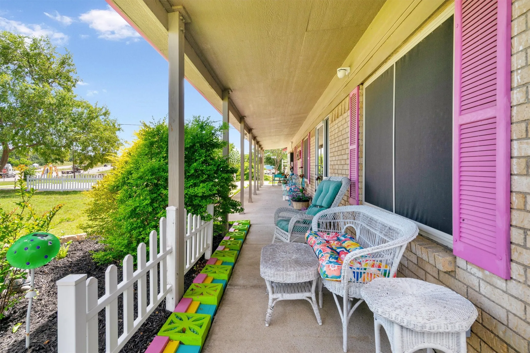 Expansive covered front porch with a brick facade and vibrant pink louvered shutters