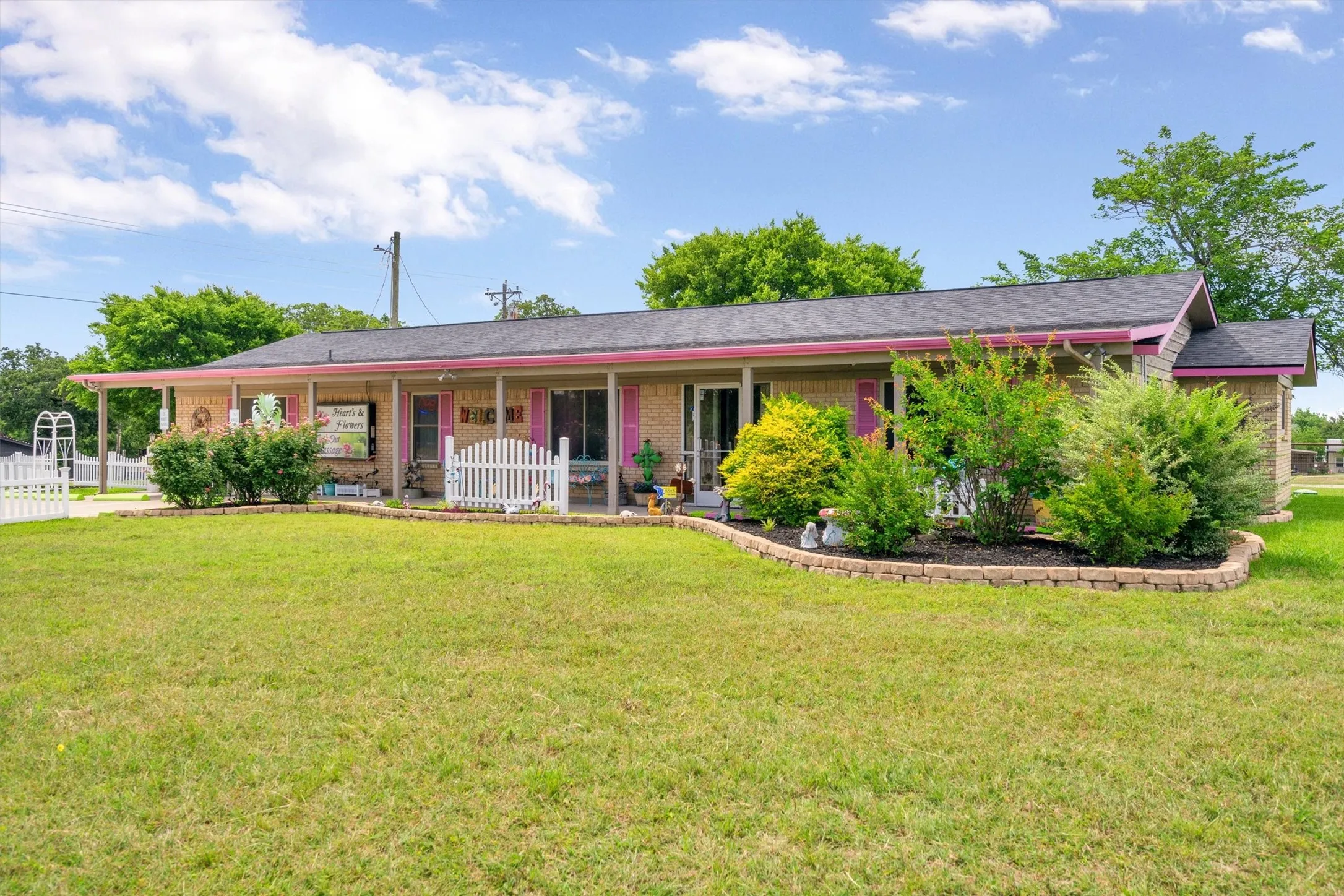 Brick exterior featuring a covered front porch, dark shingle roof, and vibrant pink trim accents
