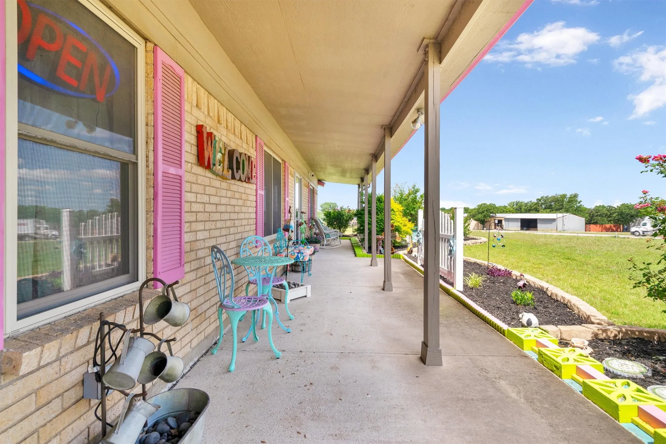 Inviting covered porch featuring a brick facade, vibrant pink shutters, and a concrete walkway