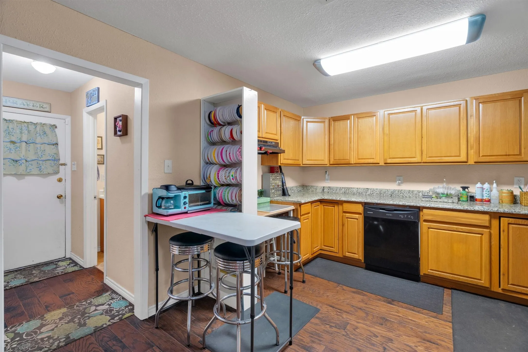 Kitchen featuring wood-finish flooring, light wood cabinetry, stone countertops, and a black dishwasher