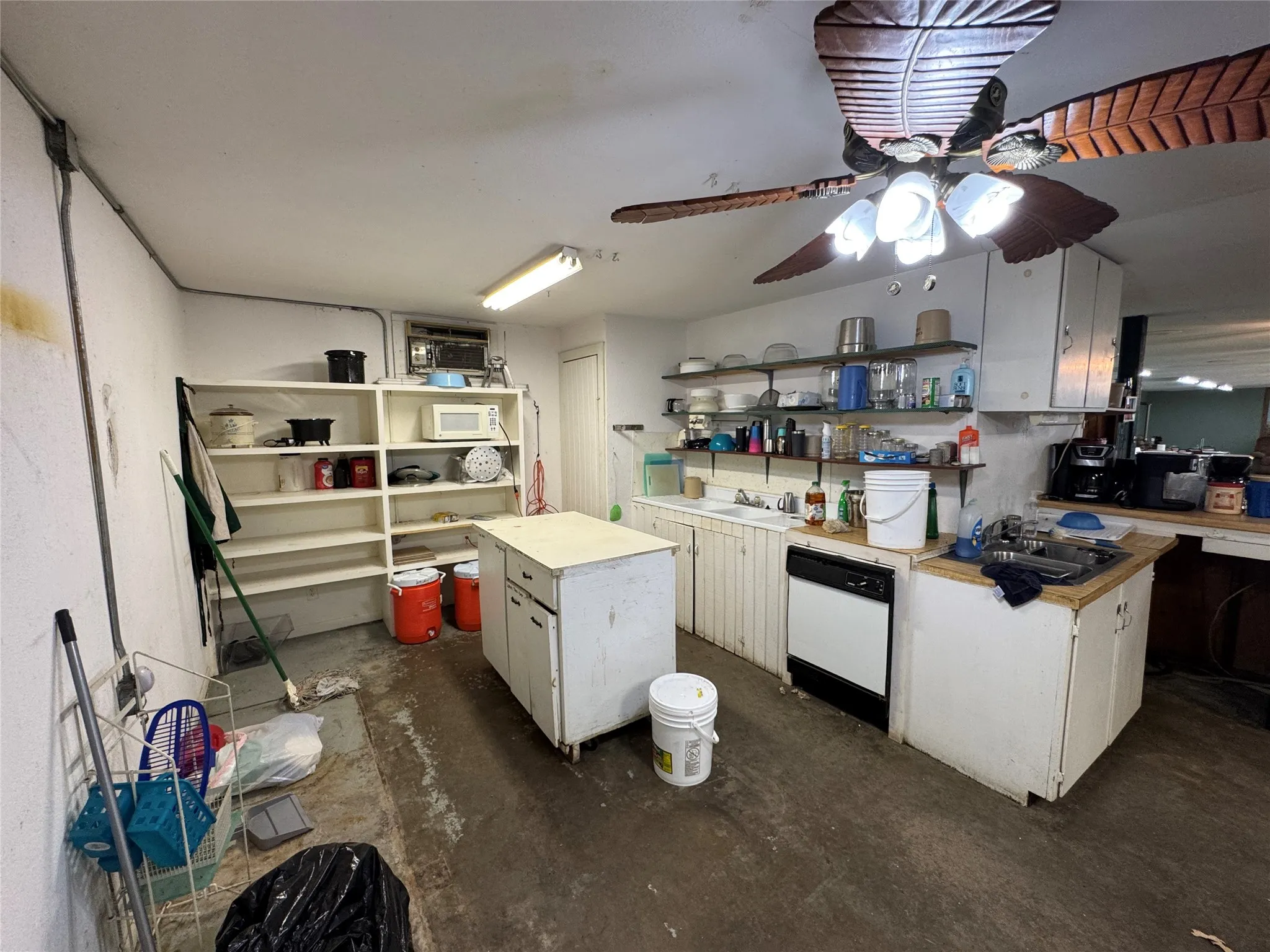 Utility kitchen featuring a built-in dishwasher, an island with lower cabinetry, open shelving, and a decorative ceiling fan with integrated lighting