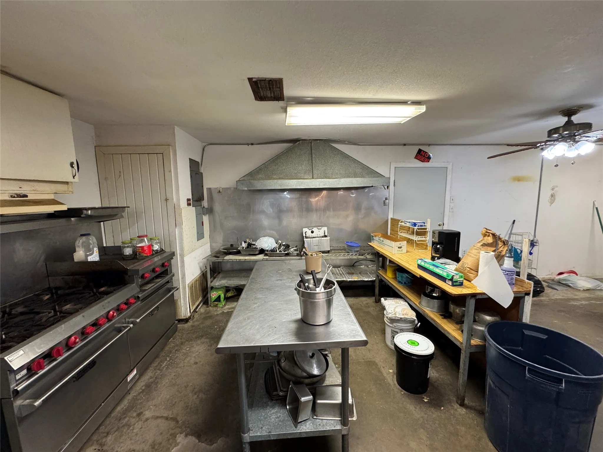 Commercial kitchen space featuring stainless steel appliances, a large ventilation hood, and extensive countertop areas