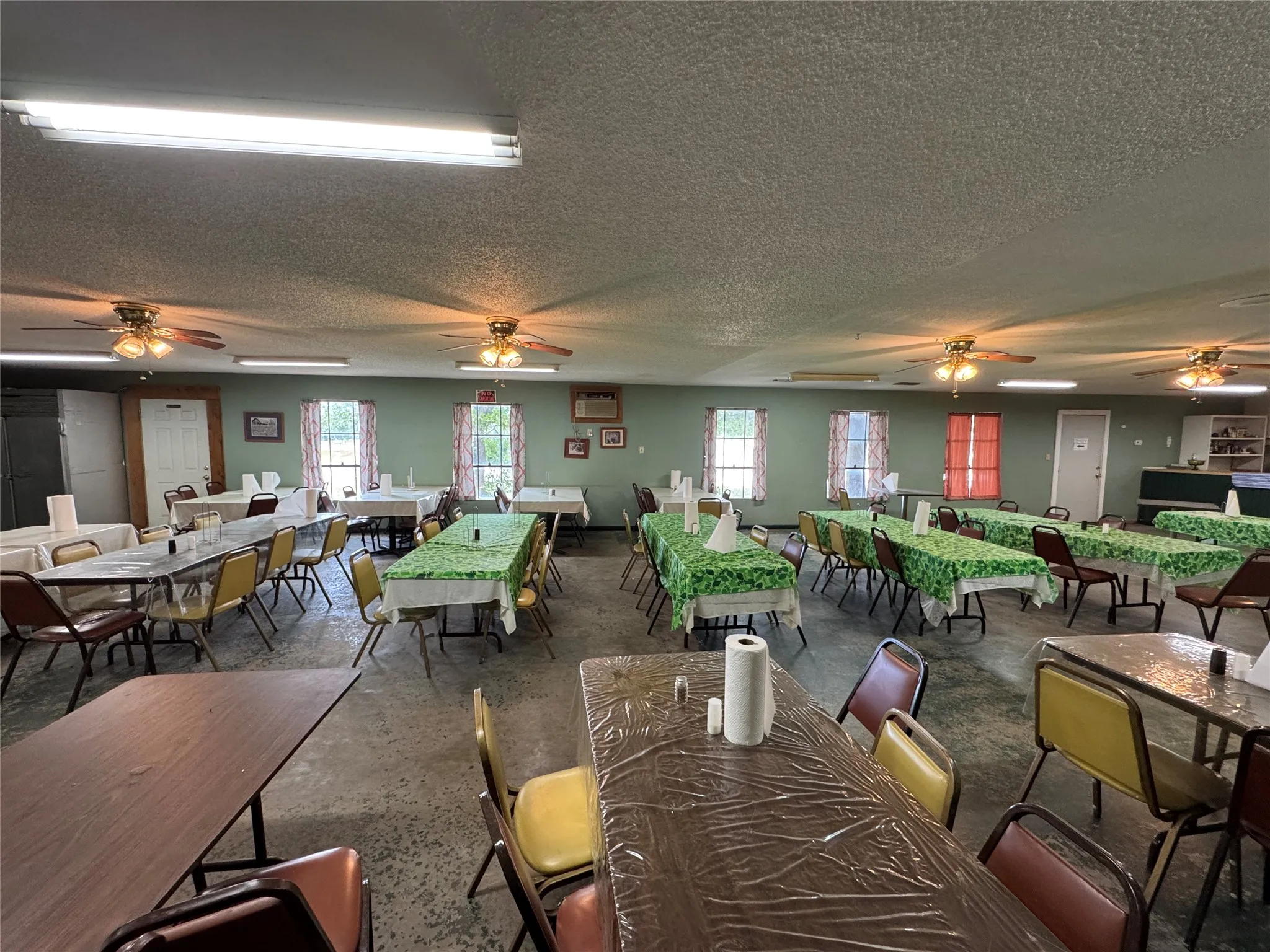 Spacious interior featuring a textured ceiling, multiple ceiling fans, and fluorescent lighting