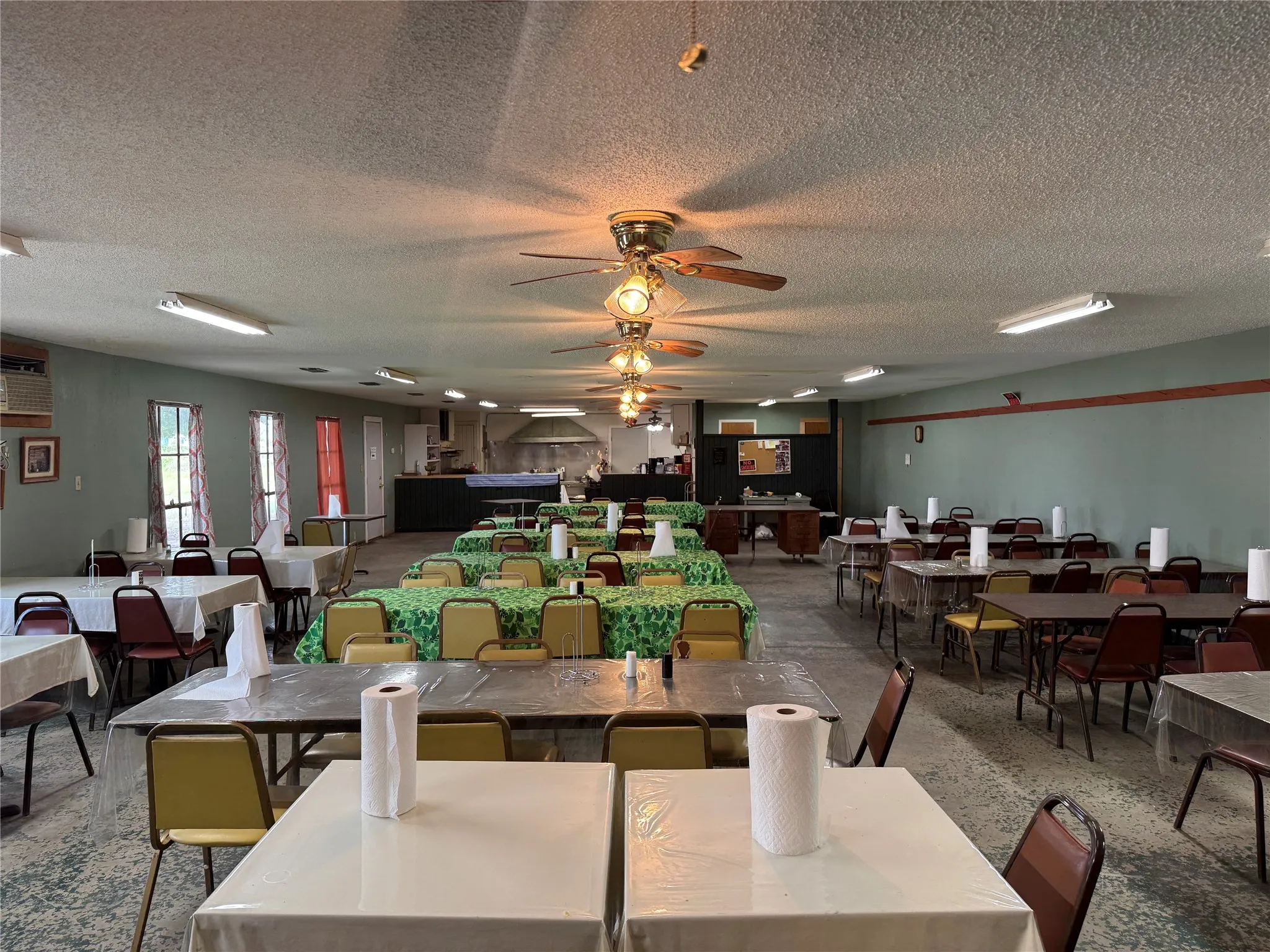 Spacious interior featuring a textured ceiling, multiple ceiling fans with light fixtures, and recessed fluorescent lighting