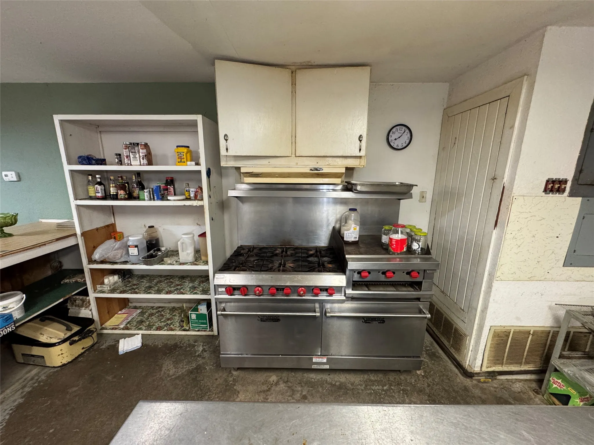 Commercial-grade stainless steel range with multiple burners and integrated ovens, beneath a professional-grade stainless steel exhaust hood