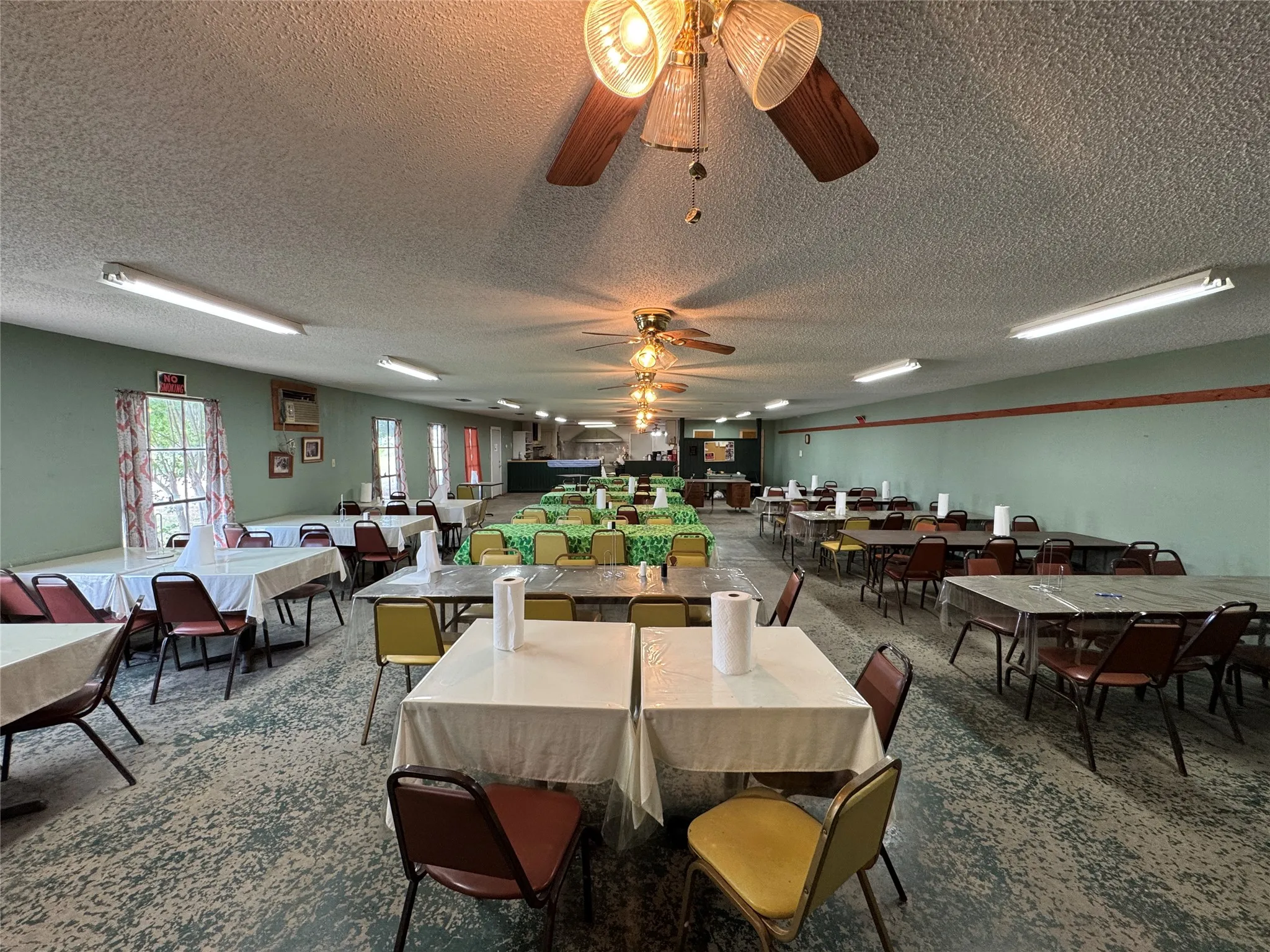 Spacious interior featuring a textured ceiling, multiple ceiling fans, and fluorescent lighting