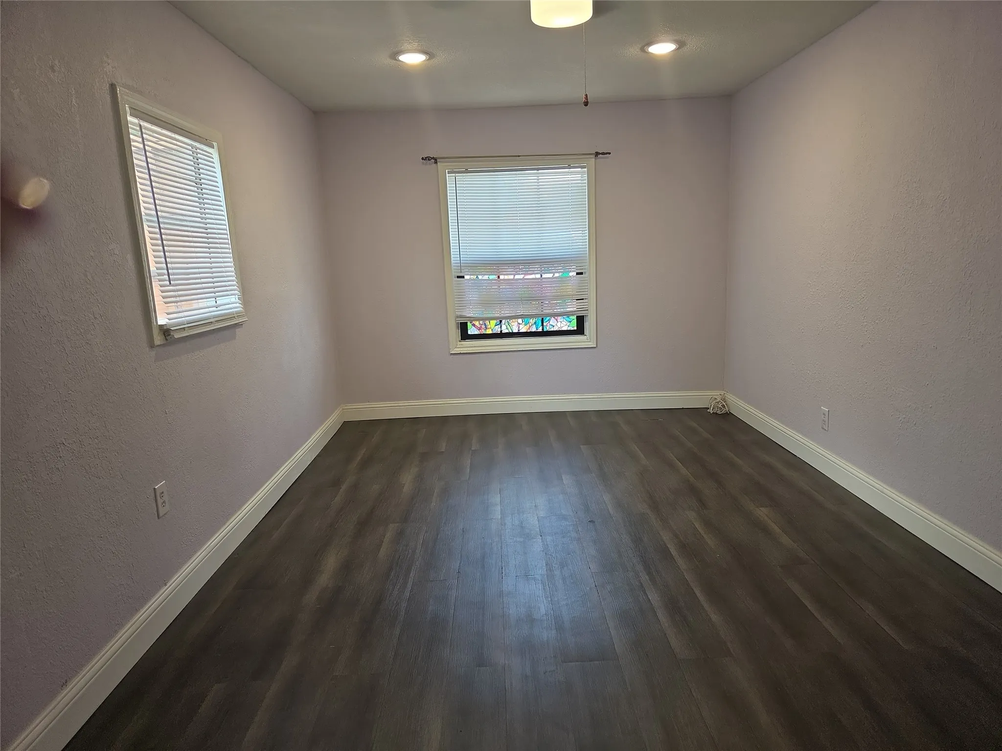 Spacious room featuring wood-finish flooring, two windows with blinds, recessed lighting, and a ceiling fan