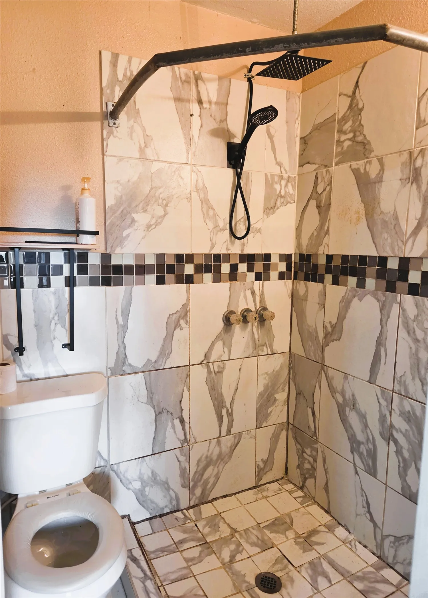 Walk-in shower featuring large format wall tiles with a gray veining pattern, complemented by a mosaic accent band
