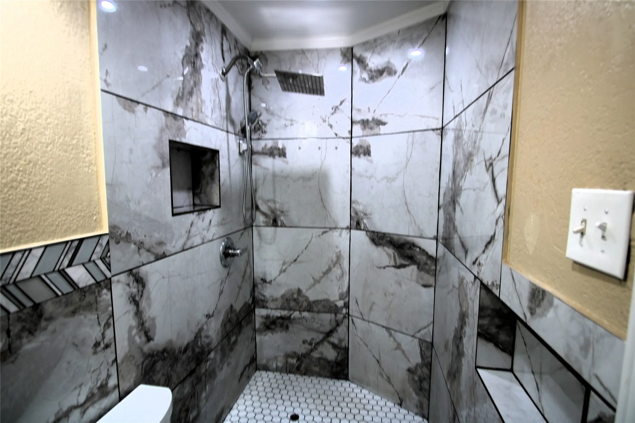 Shower featuring large format stone-finish wall tiles, a built-in shower niche, a rain shower head, and a white hexagonal tile floor