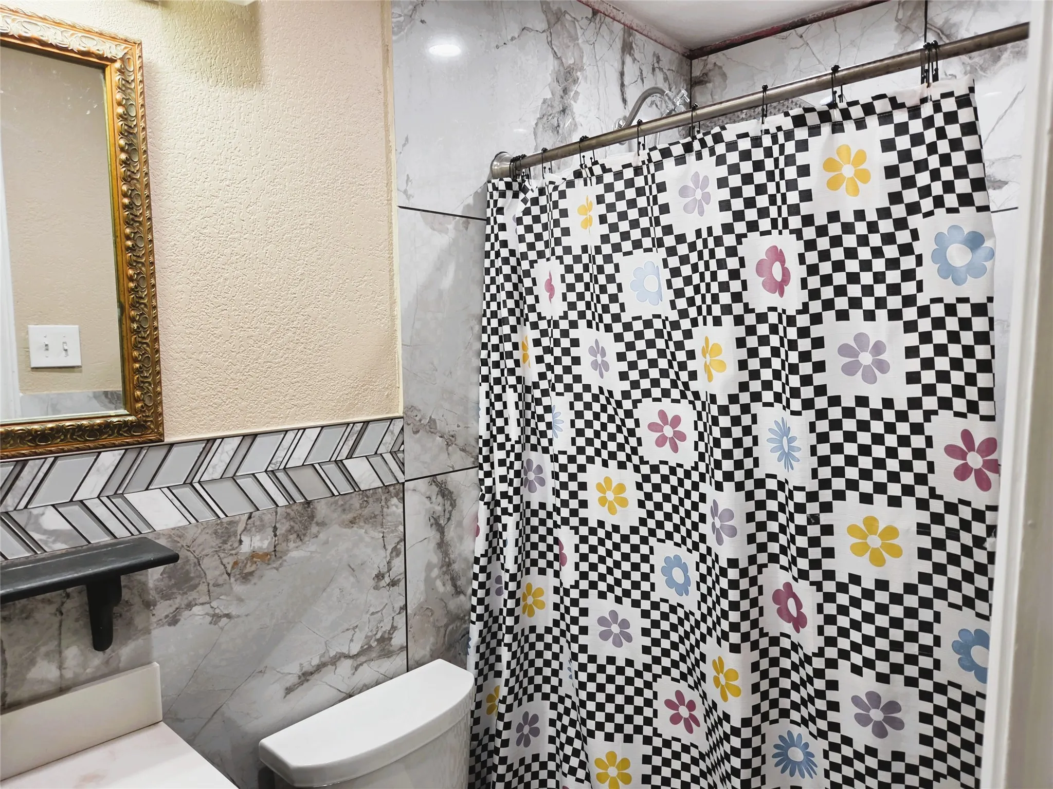Bathroom featuring a toilet, marble-look wall tiling with an accent chevron band, and a vanity with a dark shelf