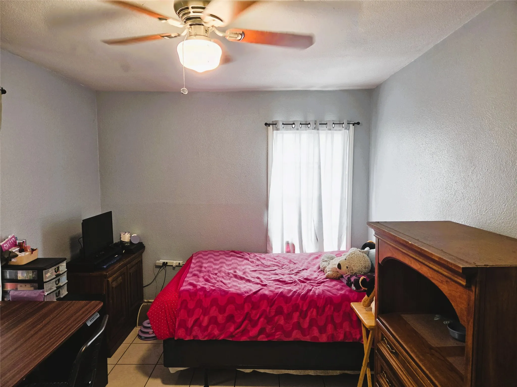 Room featuring a ceiling fan with integrated lighting, a window with white curtains, and tile flooring