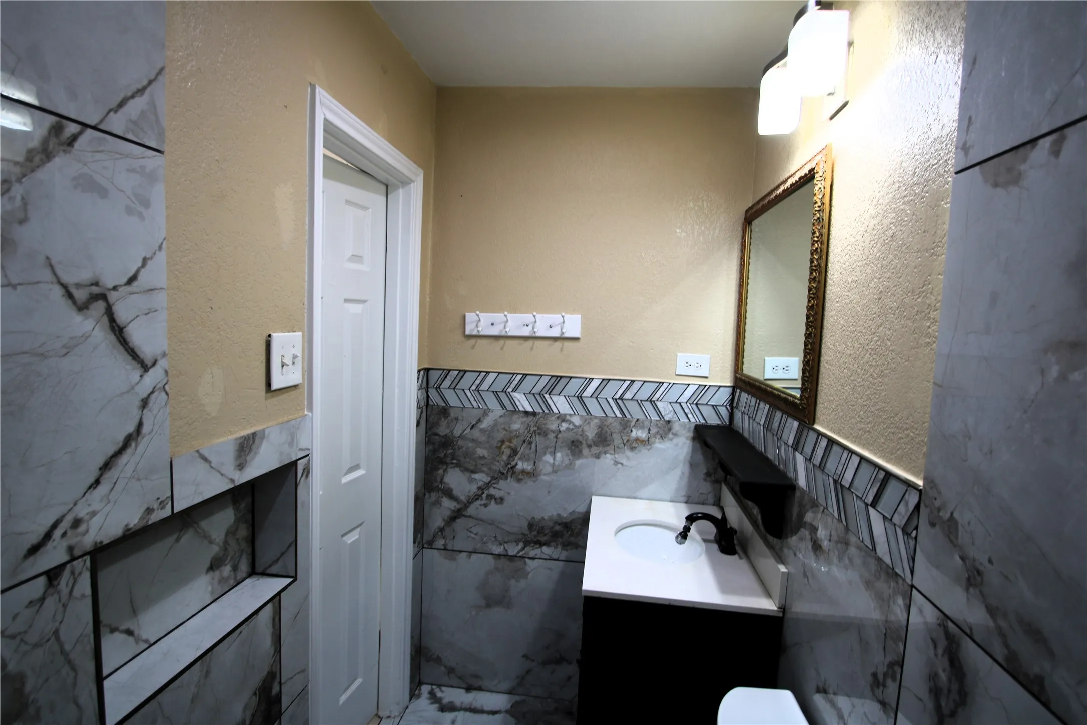 Bathroom featuring floor-to-ceiling marbled-pattern tile, a vanity with an integrated sink, a dark finish faucet, and a decorative wall mirror