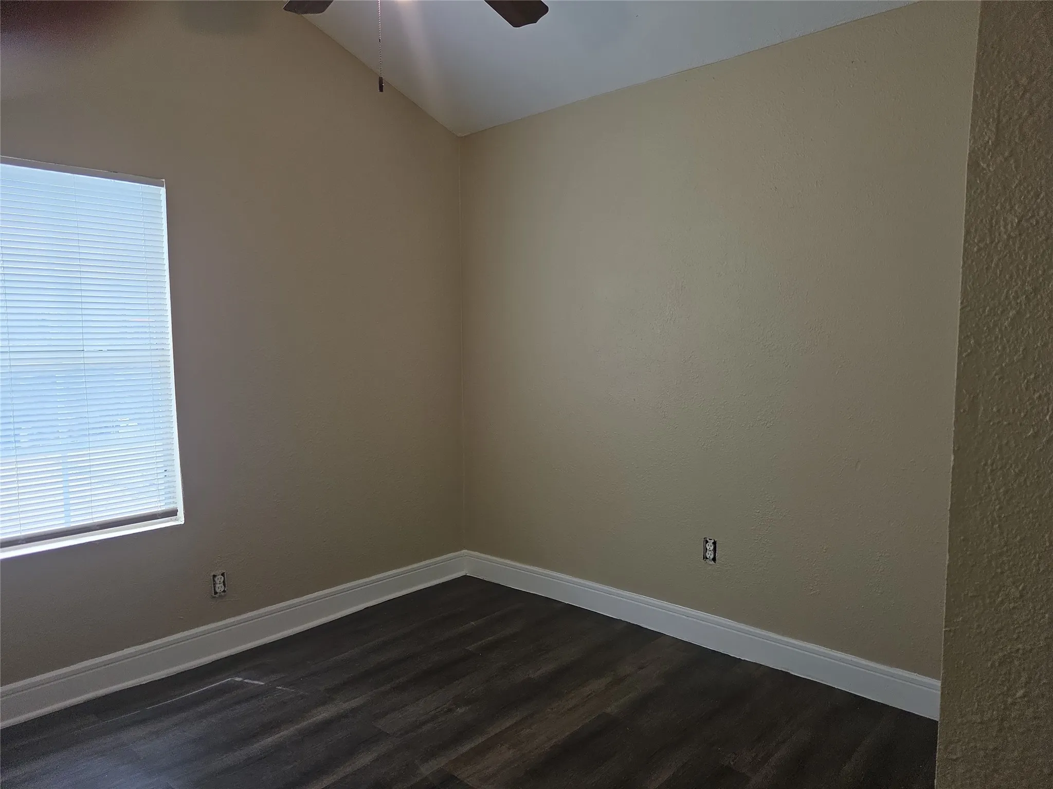 Room featuring an angled ceiling, wood-finish flooring, and a window with horizontal blinds