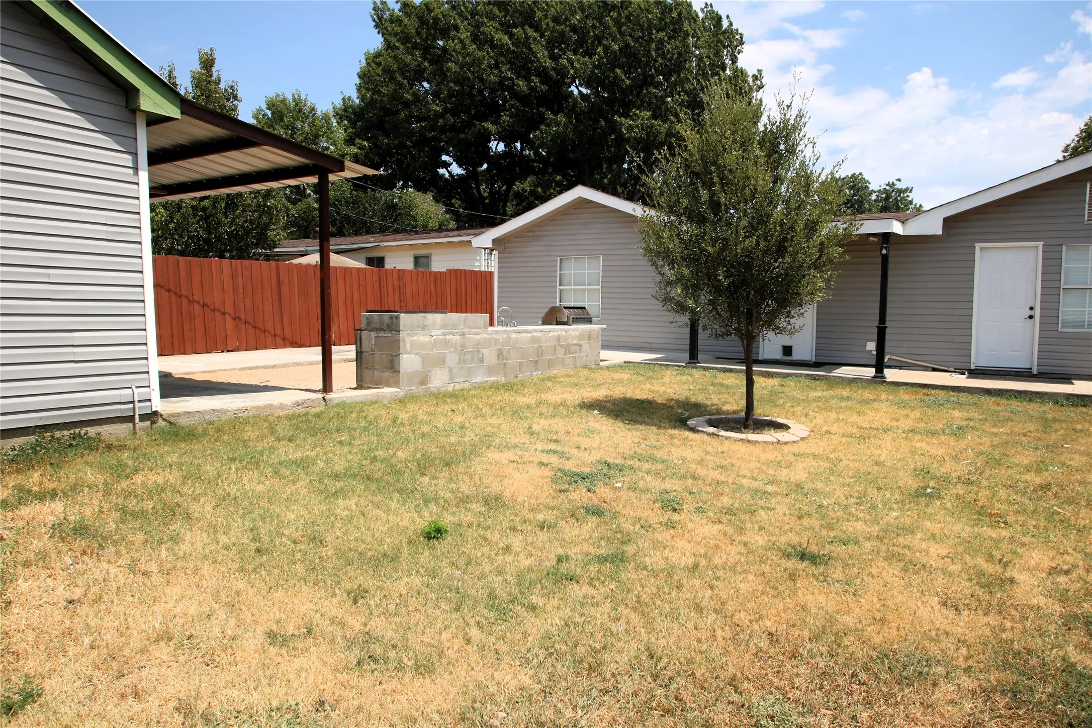 Expansive outdoor space featuring a paved patio, covered awning, concrete block planter, and mature landscaping