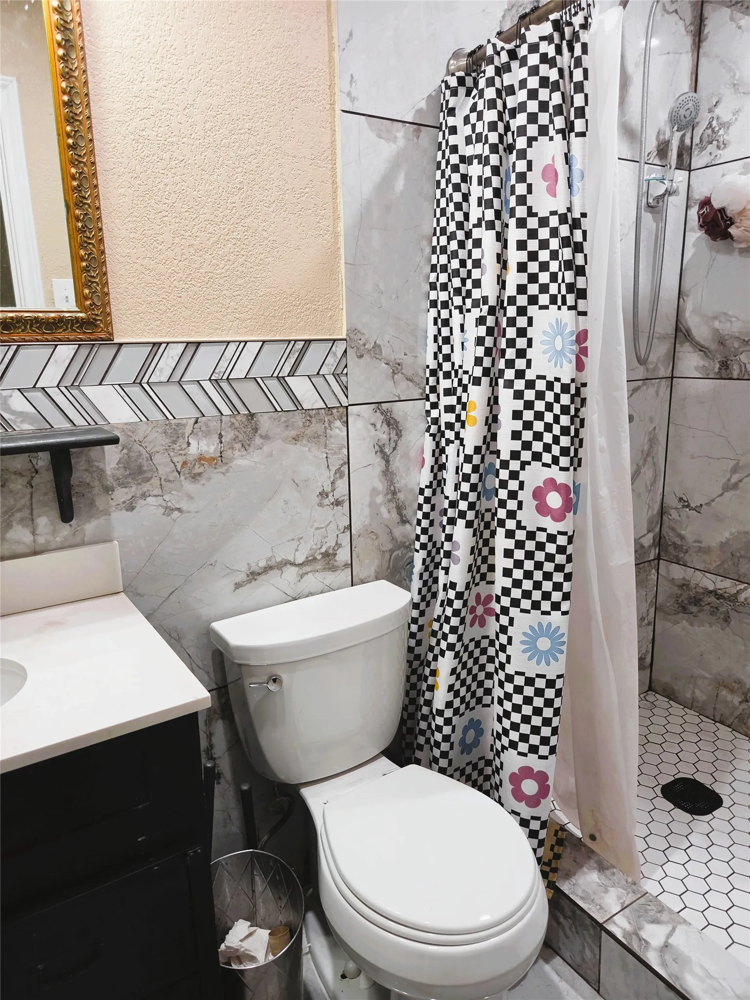 Bathroom featuring a tiled shower with hexagonal floor tiles, a vanity with a white countertop and dark cabinetry, and wall tiling with a decorative chevron accent band
