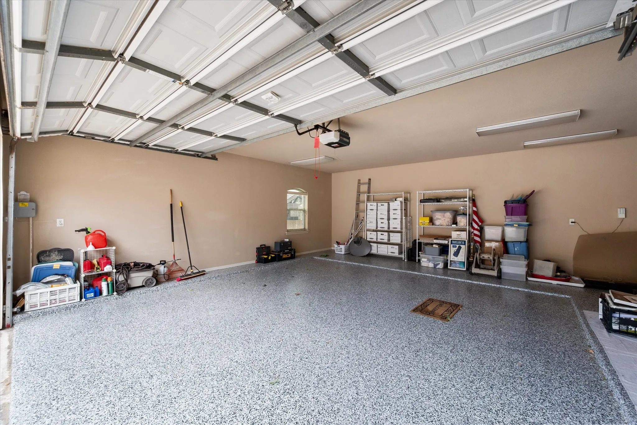 Spacious garage featuring a durable epoxy floor, an automatic overhead door opener, and integrated ceiling lighting