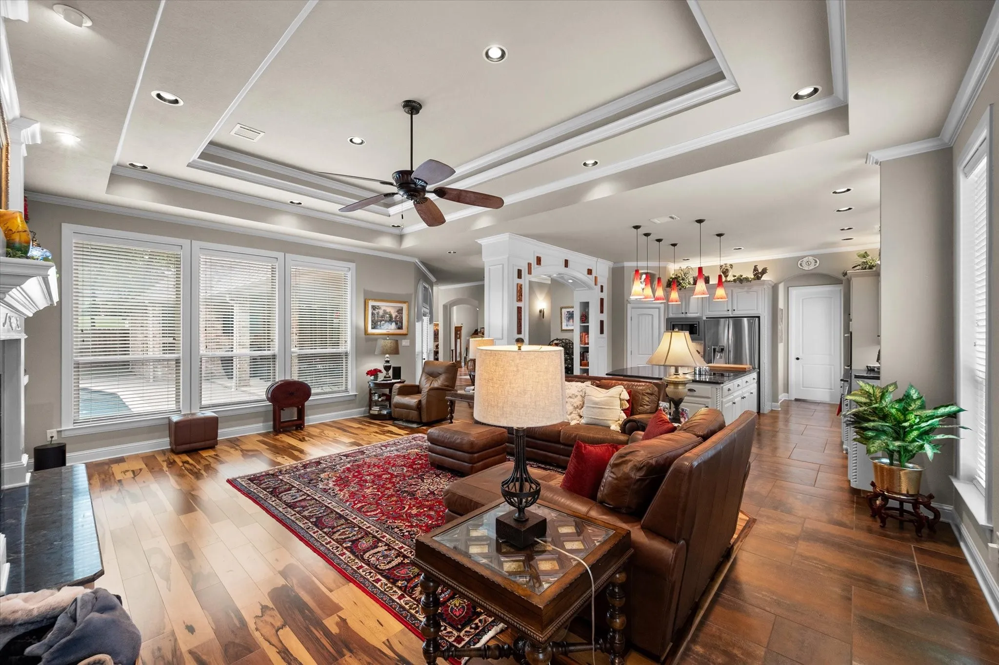 Spacious room featuring wood-finish flooring, a tray ceiling with recessed lighting and ceiling fan, and multiple windows