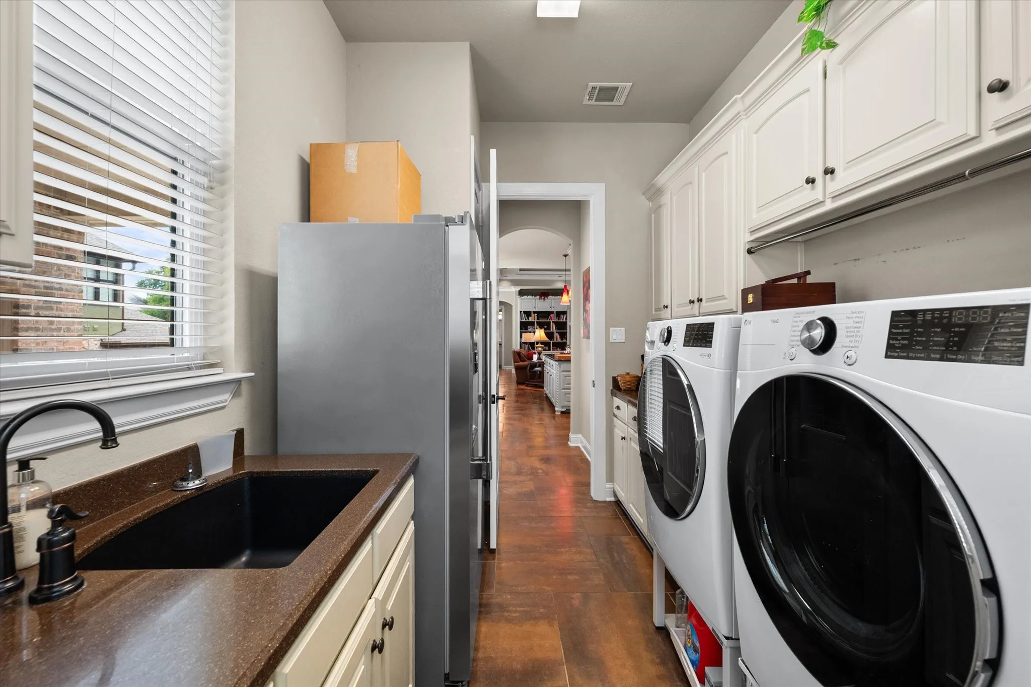 Dedicated utility room featuring abundant cabinetry, a built-in sink with a dark faucet, wood-finish flooring, and a window with blinds