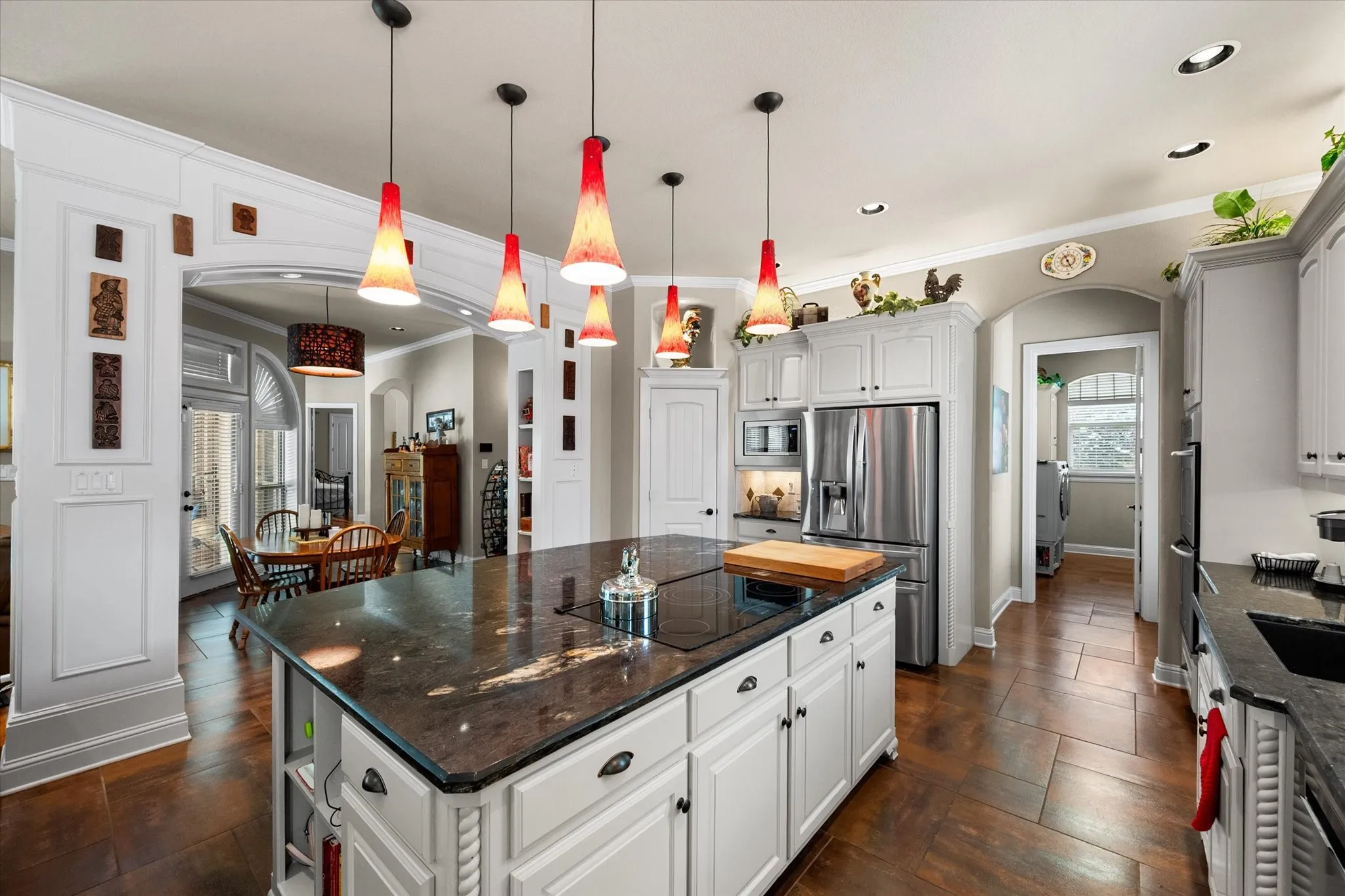 Spacious kitchen featuring a large central island with a cooktop, white perimeter cabinetry, stainless steel appliances, and dark stone countertops