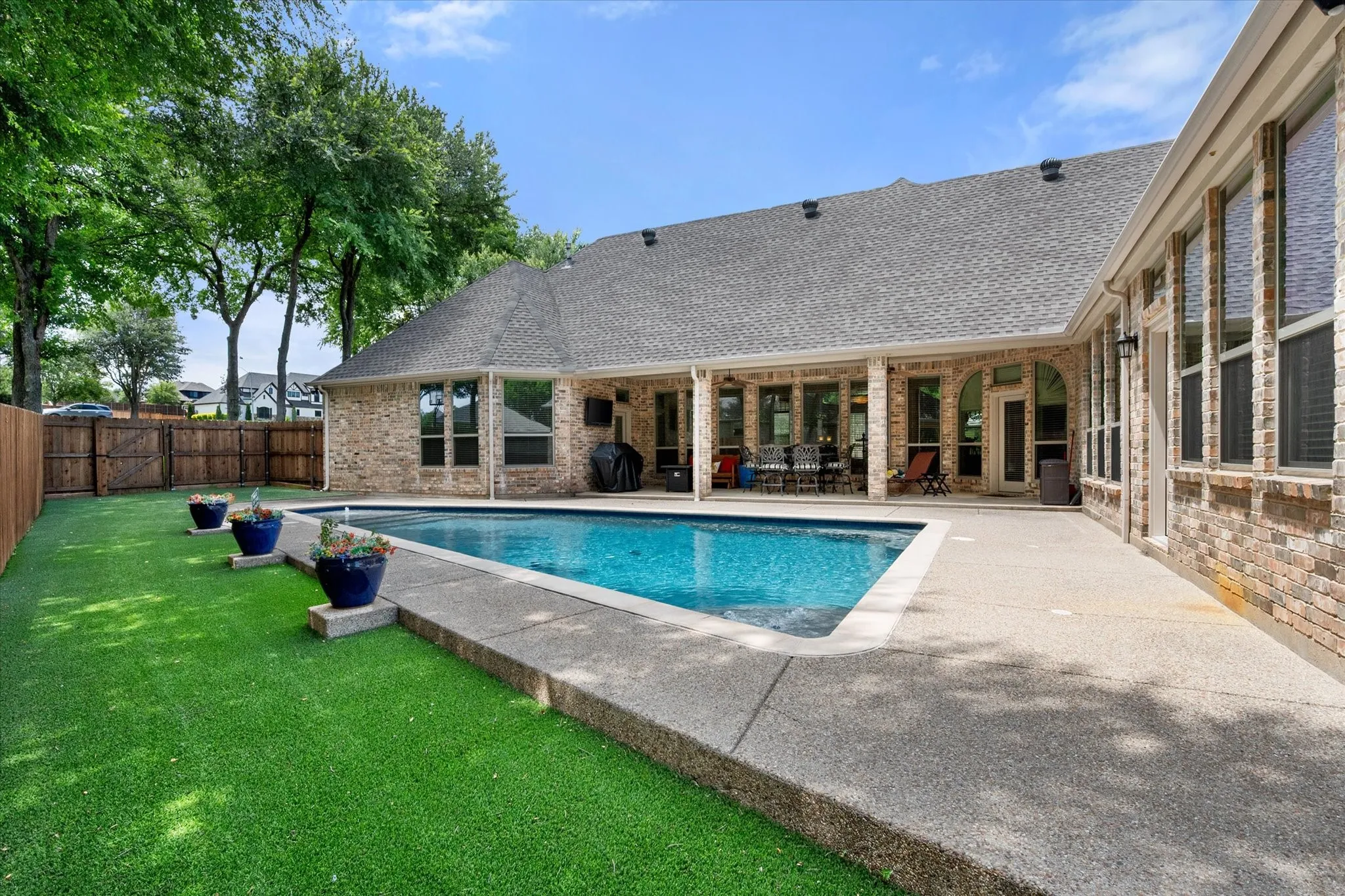 Inviting backyard oasis featuring a rectangular swimming pool, concrete patio, and artificial turf lawn