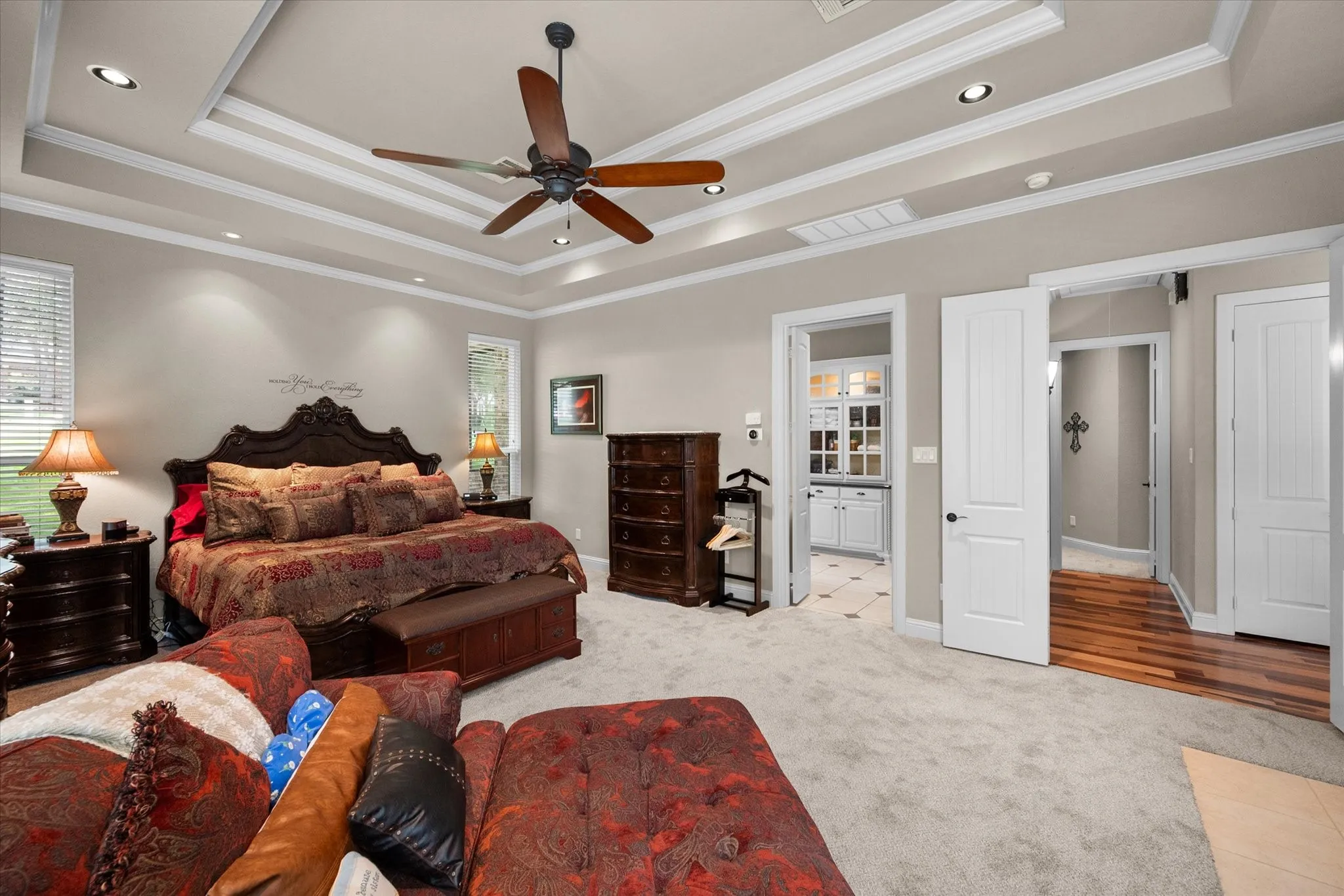 Spacious room featuring a tiered tray ceiling with recessed lighting and a ceiling fan, plush carpet flooring, and multiple doorways including one to an adjacent room with patterned tile flooring