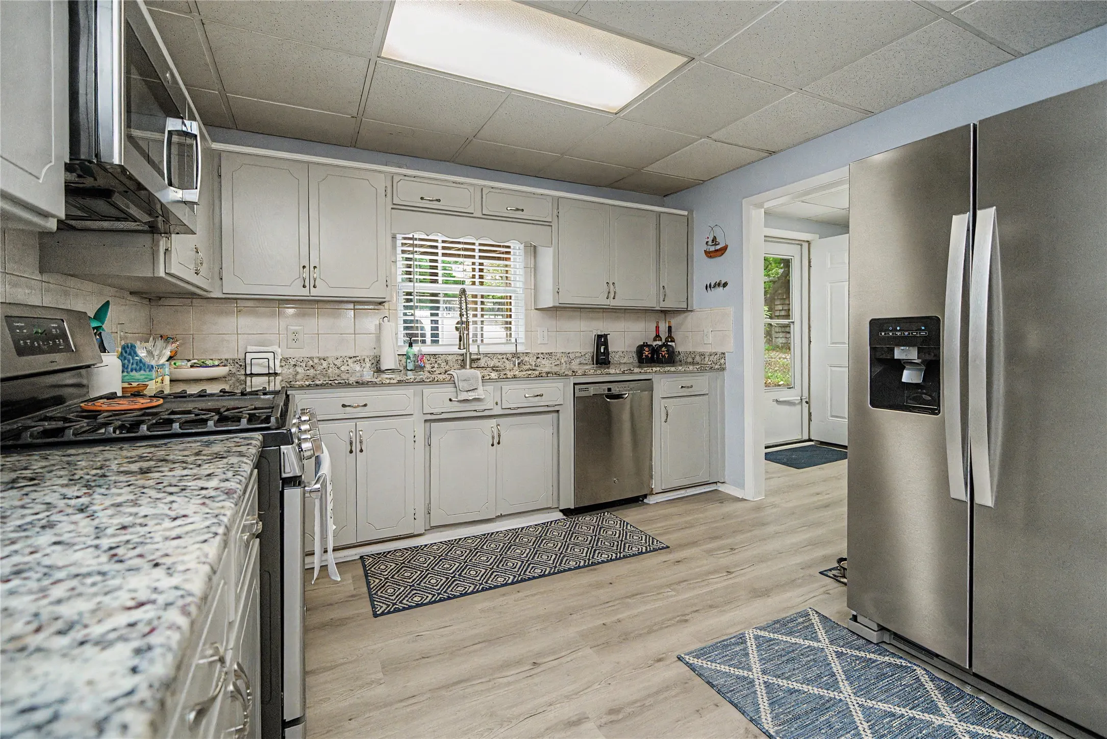 Kitchen featuring light gray cabinetry, stainless steel appliances, speckled stone countertops, and wood-finish flooring