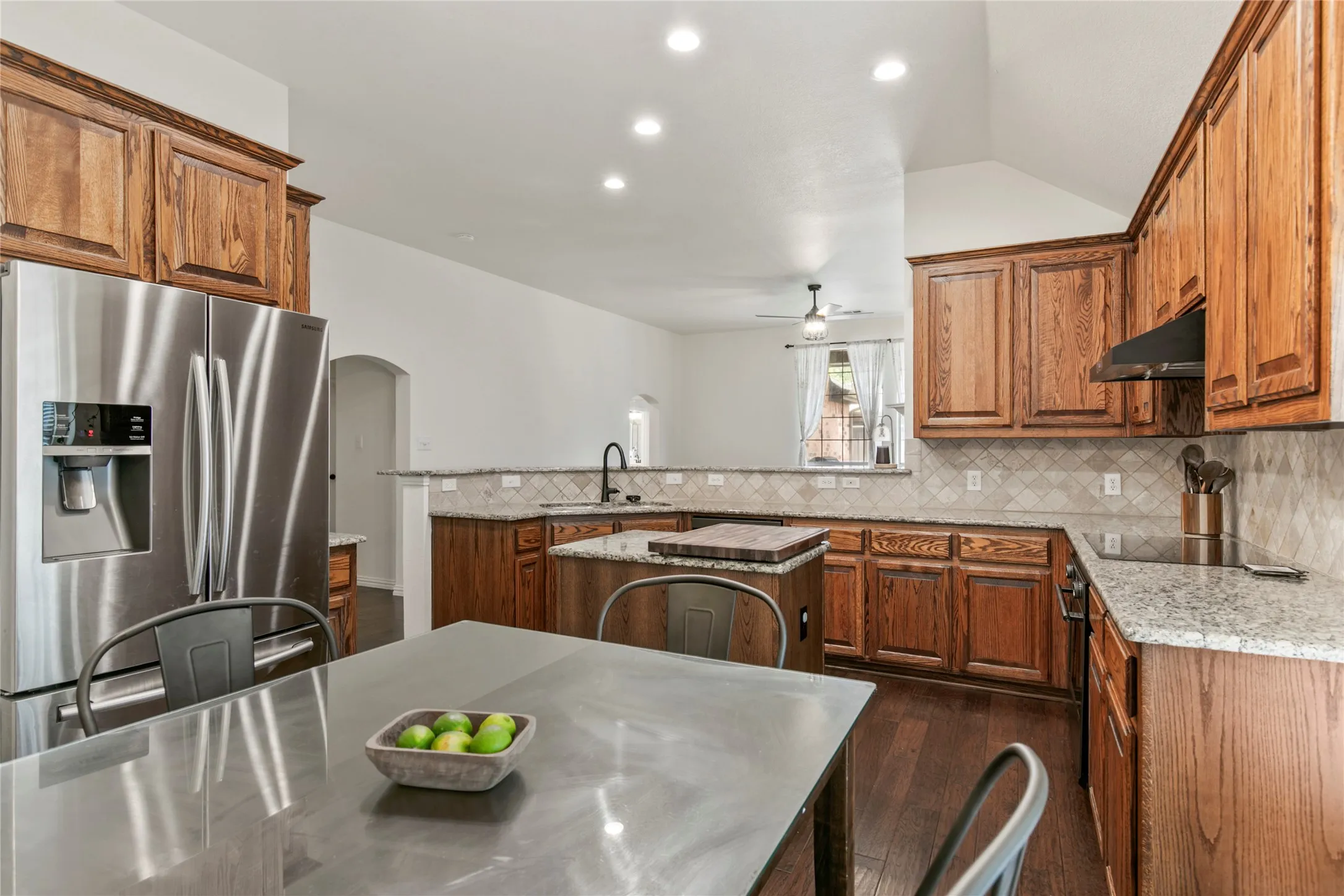 Kitchen featuring wood cabinetry, stainless steel appliances, granite countertops, tile backsplash, and dark wood-finish flooring