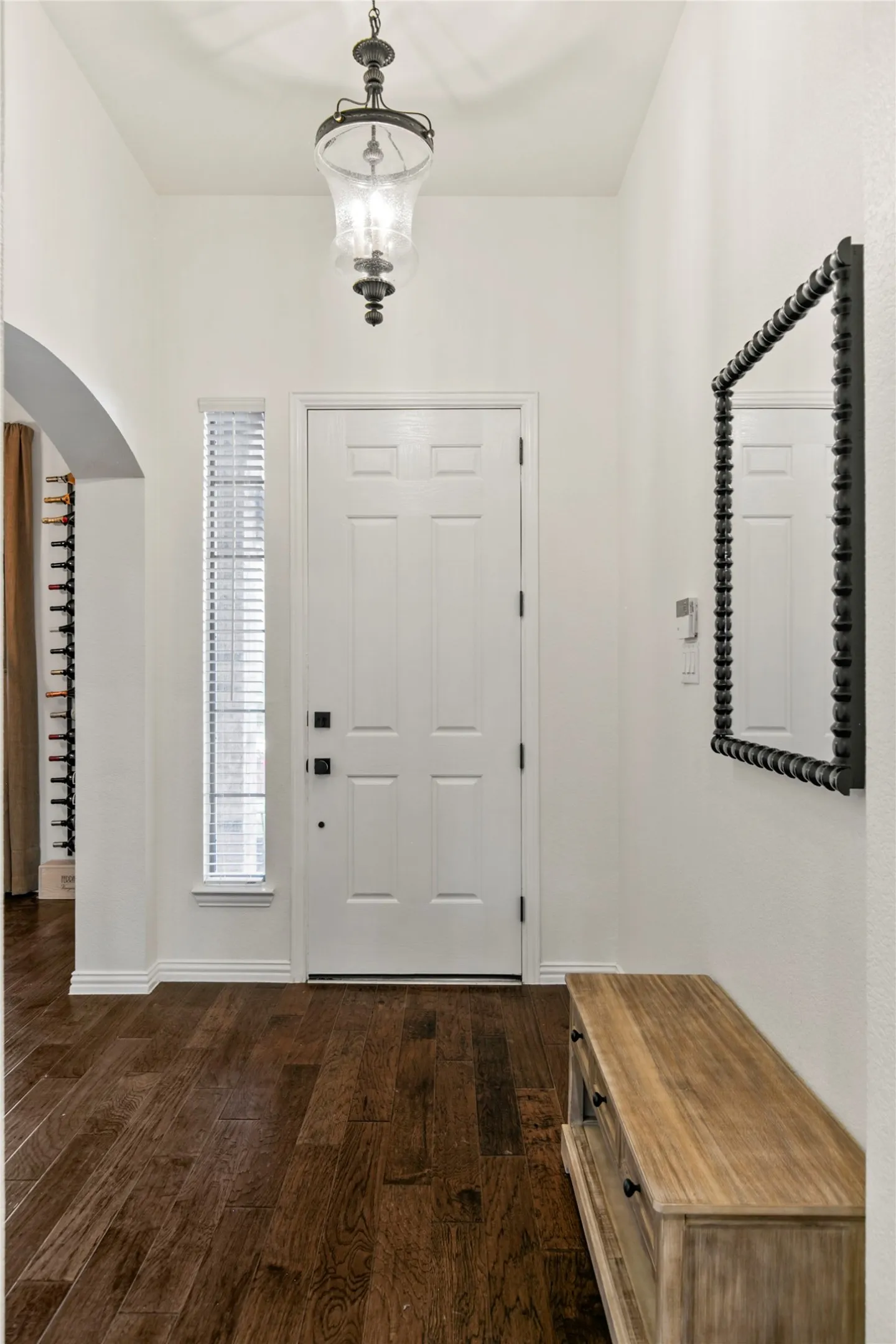 Entryway featuring rich wood-finish flooring, a white paneled door with dark hardware, and a hanging pendant light fixture